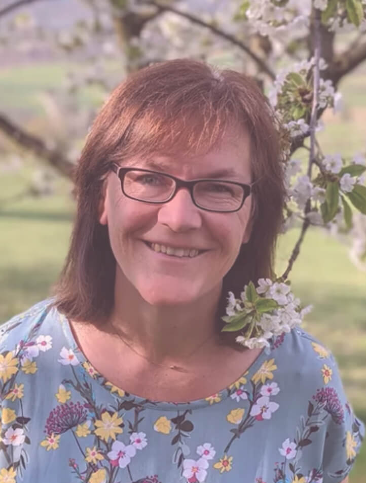 Lächelnde Frau mit Brille vor blühenden Bäumen – femfeel Nutzerin Natascha teilt ihre Erfahrung.